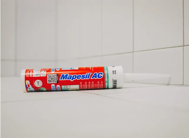 Silikonový tmel Mapesil AC na bílých obkladech.
