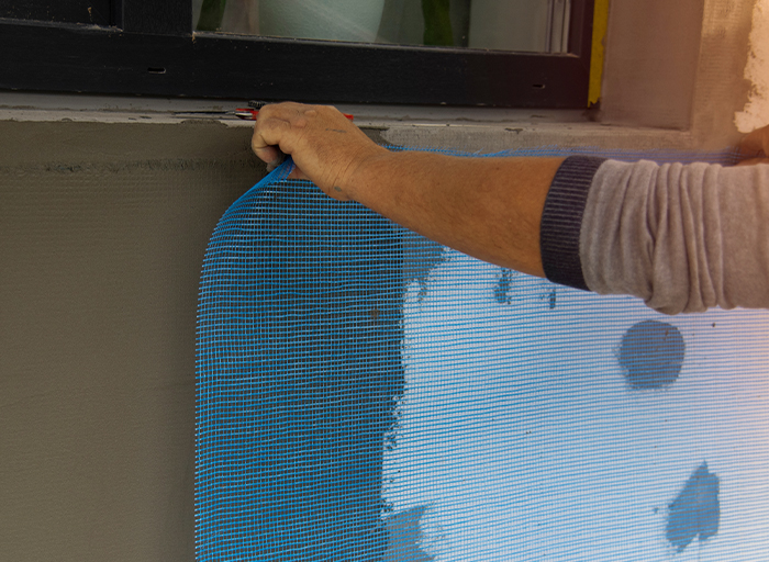 Technik upevňuje perlinku na fasádu před nanášením lepidla při zateplování budovy.