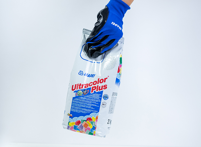 Ruka v rukavici drží balení spárovací hmoty Ultracolor Plus od MAPEI.